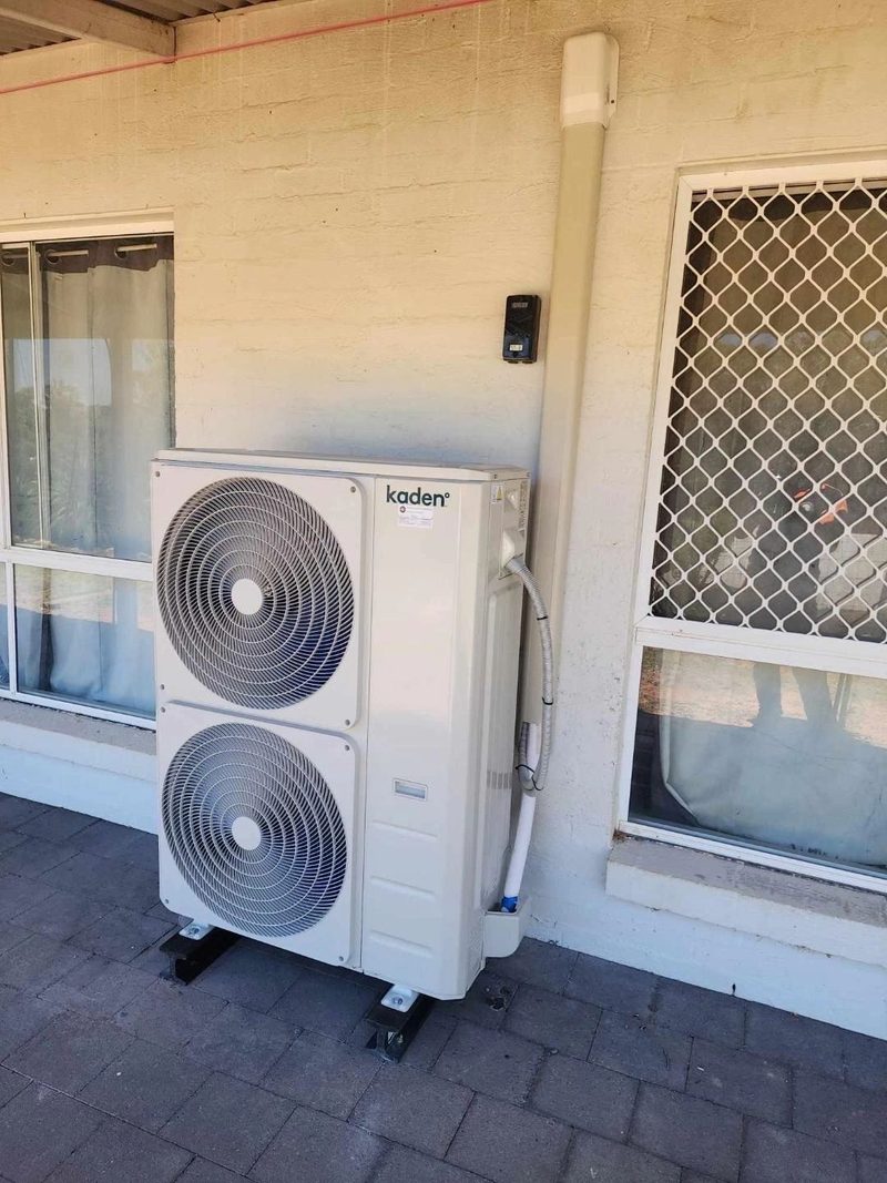 Twin fan outdoor unit on levelled feet beside a home